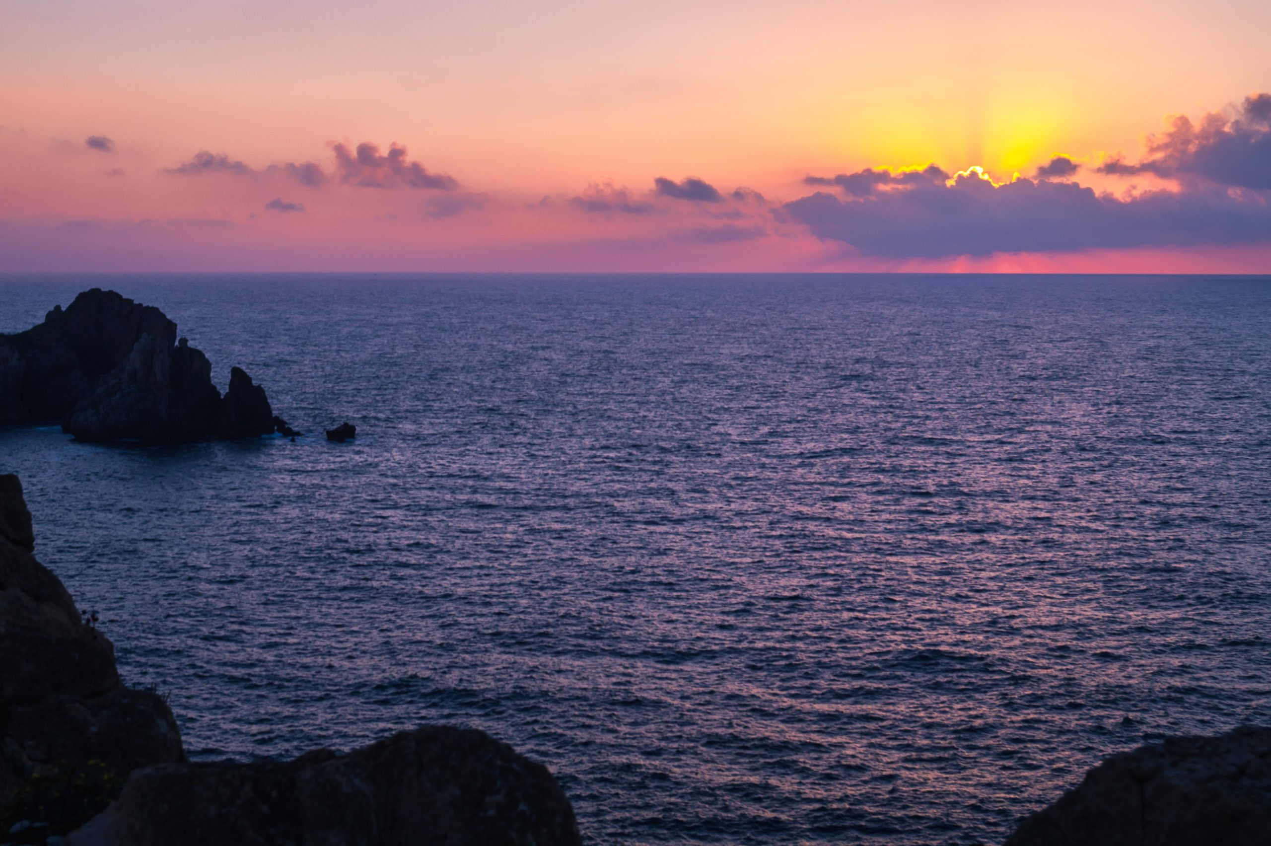 Sunset with sun, clouds and calm sea on cliffs of Costa Quebrada